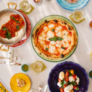 Looking down on a vibrant lunch table at Caruso Grill with pizza, vegetables, pasta and beans on bright ceramic plates.