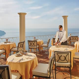 Classic Tuscan columns border a large restaurant balcony open to the sky with views of the Lattari Mountains and sea