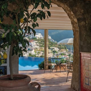 Strings of onion and garlic hang above a Ravello-tiled bar. A blue infinity pool leads the gaze to a hillside dotted with homes