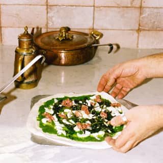 A chef prepares a pizza with a pesto-green base, mozzarella and ham on a marble counter in the Pool Grill kitchen.