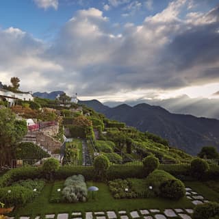 Neatly manicured Italian gardens dotted with stone paved paths beside a hilltop villa