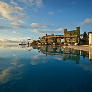 Classic Tuscan columns, ivy clad walls and the lightest puff of clouds are reflected in the blue stillness of an infinity pool