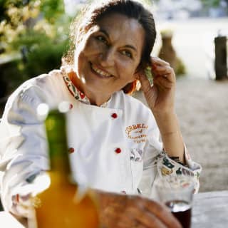 Italian chef, Giovanna Voria, smiles as she drinks an aperitif. Her chef's whites are branded Corbella, decorated with red buttons