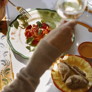 Seen from above, a guest raises a glass of white wine above a vibrant plate of spaghetti Ravello with tomatoes and basil.