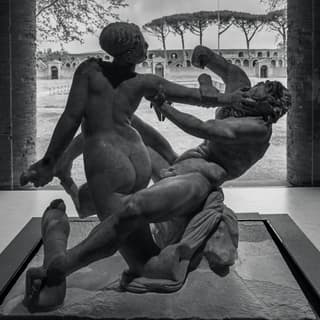 Black and white image of a marble statue of a man and woman fighting encased in a glass frame in Pompeii