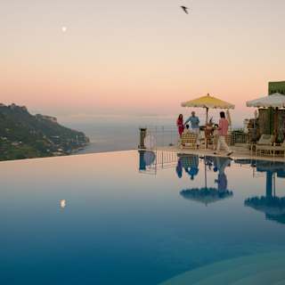 A reflection of the moon in a peach sky settles on the still water of the infinity pool as four guests enjoy poolside drinks.