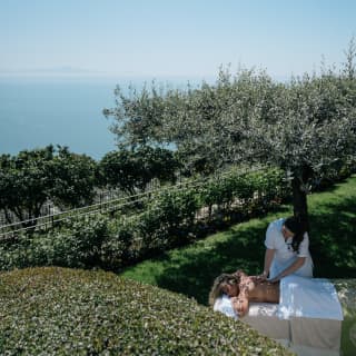 The silver-toned leaves of an olive tree in a private garden provide dappled shade for a masseuse and her client