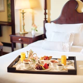 Room-service breakfast tray laden with breakfast dishes placed on a pillowy bed