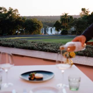 In soft-focus, a waiter pours rosé into glasses at a table on Itaipu's balcony with brilliant views of the Iguassu Falls.
