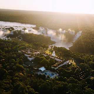 Aerial view of Hotel das Cataratas nestled in forest opposite the magnificent Iguassu falls, illuminated by sun.