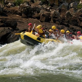 A yellow inflatable raft with passengers paddling against white water rapids