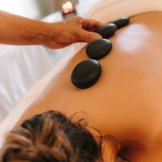 A member of the spa staff places smooth black pebbles along the spine of a female guest during a hot stones massage.