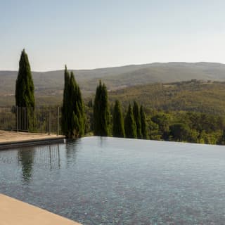 Glistening with blue mosaic tiles, the infinity pool falls into extraordinary views of rolling Tuscan hills and cypress trees.