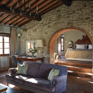 A red brick arch in a stone wall connects an exquisite traditional Tuscan sitting room with a sumptuous bedroom