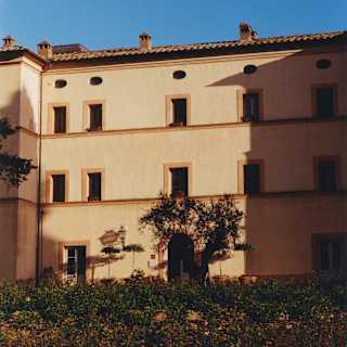 View over gardens of the exterior of Casello di Casole with three levels of doors and windows in warm honey-toned walls.