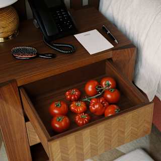 A group of nine beef and vine tomatoes sit in the open bedside draw of a bedside table, seen from above in a room detail.