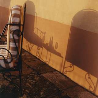 The shadows of filigree chair frames and a table with drinks create pretty curls and shapes on an ochre-rendered wall.