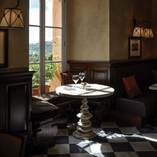 Light falls on a table with two wine glasses tucked in a bay window at Bar Visconti, with banquettes and chequerboard tiles.