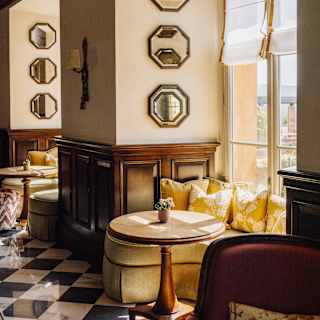 A round table with a gold-tone crescent banquette catches sun in a window alcove in the cool interior of Bar Visconti.