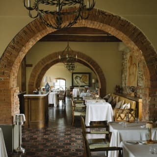 View of three clothed tables in the foreground of Tosca restaurant with more beyond, seen through rustic brick wall-arches.