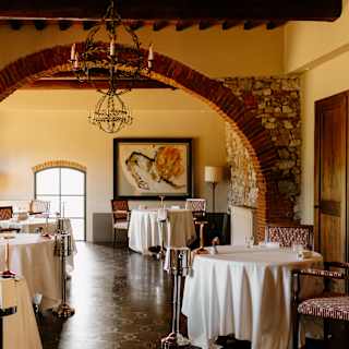 View of white-clothed tables with wine stands in the honey and stone dining room, spanned by a wide brick wall arch at Tosca.
