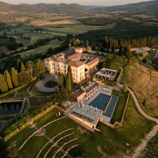 Aerial view of Castello di Casole as late sun throws soft gold light on its grassy amphitheatre, pool and impressive estate.