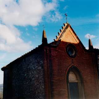 In a low-angle view of the Castello di Casole chapel, mainly in shade, rising into a blue sky, the pediment catches the sun.