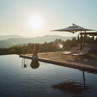 The setting sun casts a terracotta planted ball shrub and white parasol into black silhouettes on the surface of the pool