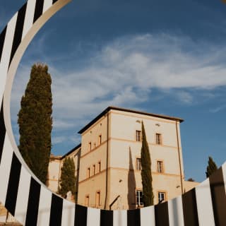 Low-angle image of the honey-toned Castello di Casole, seen through the black and white-striped MITICO portal sculpture.