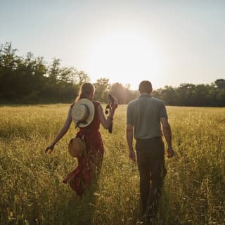 Lady in a red dress walking through a grassy field with a guide at sunrise