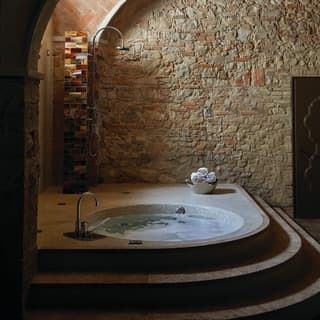 Circular hot tub in a rustic, underground, stone-walled spa
