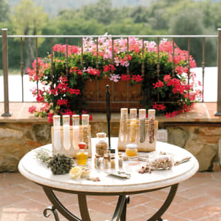 Test tubes of dried petals, rock salts and herbs stand on a garden table laden with honey, oil, bathbombs and dried rose buds