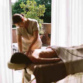 A spa therapist massages a woman half-covered with a sheet as she lies face-down on a massage bed, in soft-focus.