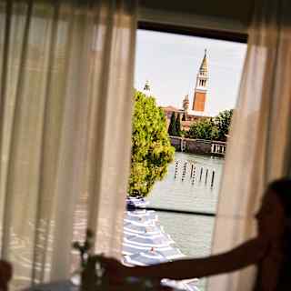 A couple inside a suite, in low light, enjoy breakfast by a window with crisp views over the canal to San Georgio Maggiore.