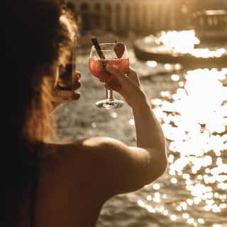 Una donna che brinda con un cocktail mentre il sole tramonta su Venezia