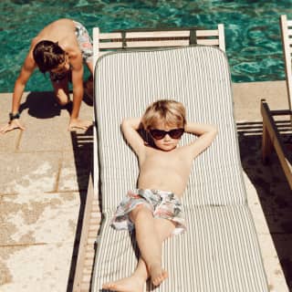 Young boy wearing sunglasses and relaxing on a sunbed beside an outdoor pool