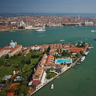 An aerial view captures the red roofs, gardens and blue pool of the Cipriani in the foreground with Venice’s main island behind