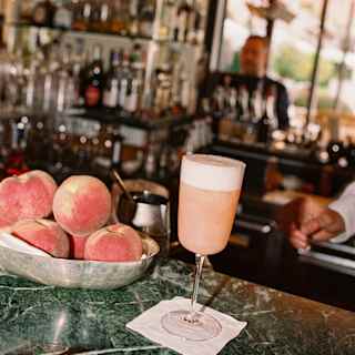 A pink Peach Bellini cocktail rests on a napkin next to a bowl of peaches on the green marble bar top at Il Bar Gabbiano.