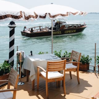 A table for two is set at the water’s edge, shaded by a hazel-trim white parasol. The Hotel Cipriani’s private launch passes by