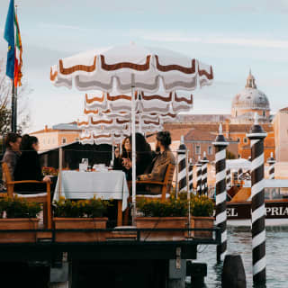 Hotel Cipriani guests dine al-fresco paraded by striped mooring poles with the Church of San Giorgio Maggiore rising behind.