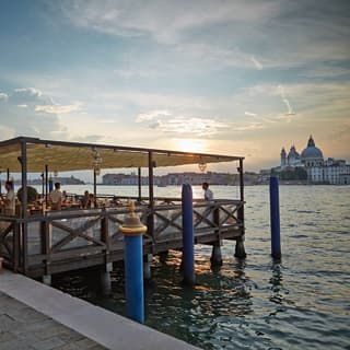 Floating restaurant on a pier extending onto the Venice Lagoon under a dramatic sunset sky