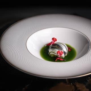 Evoking the Italian Tricolore, this fish dish is served in a white wide brimmed bowl with green broth and red petal garnish