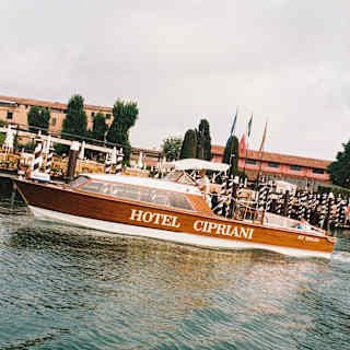 The Hotel Cipriani shuttle boat waits by the black and white paline moorings, in an angled image from the water.