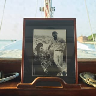 A framed black and white photo of a man and a woman stands propped up in pride of place on the foredeck of a wooden yacht