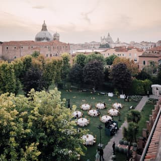 Circular banquet tables on a manicured lawn surrounded by trees in the heart of Giudecca, Venice