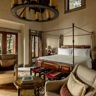 Diagonal view across the Presidential Casita, over two beige chairs and a coffee table to a bed with windows, left and above.