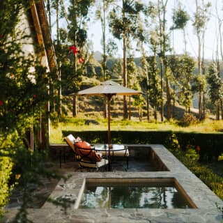 A terrace with a seating area and square plunge pool nestles in greens of the countryside, with lush grass and tall trees.