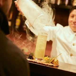 A barman in white creates theatre as he lifts a smoke cloche from a tall pisco-like cocktail on the bar top at Piccq'io.