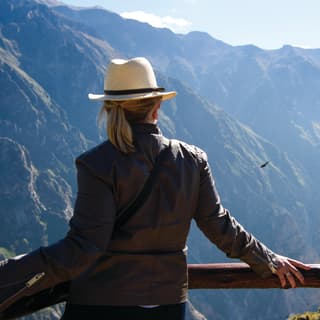 Lady in a brown leather jacket and Panama hat watching flying condors