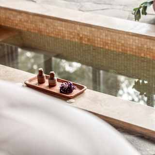 A clay tray with two small bottles and a botanical clipping rests on the edge of a rectangular plunge pool, seen in close-up.